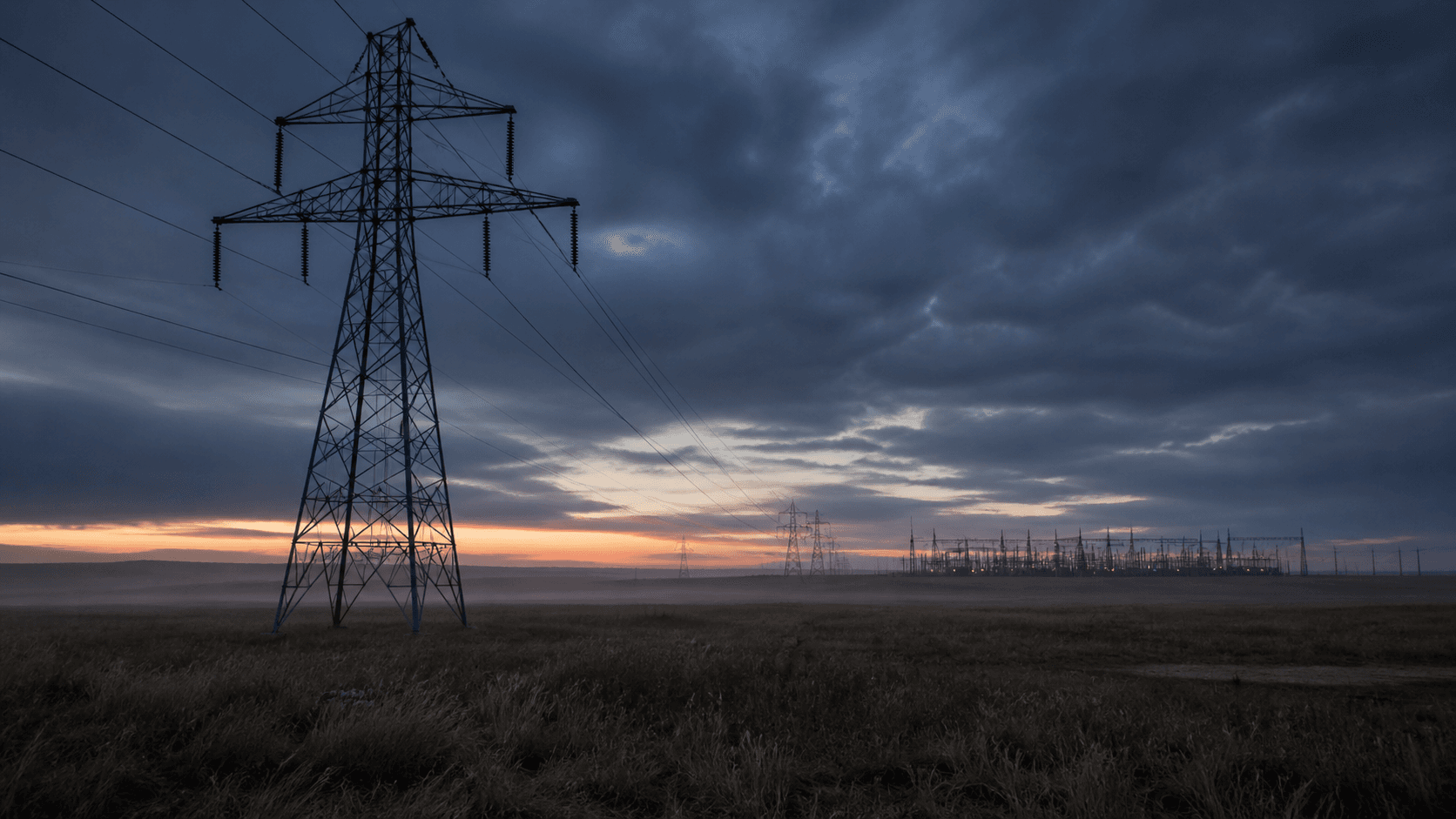 High-voltage transmission infrastructure crossing open land at dawn